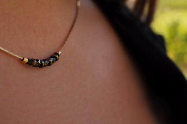 Image portée du collier noir et doré monté sur une chaîne fine dorée