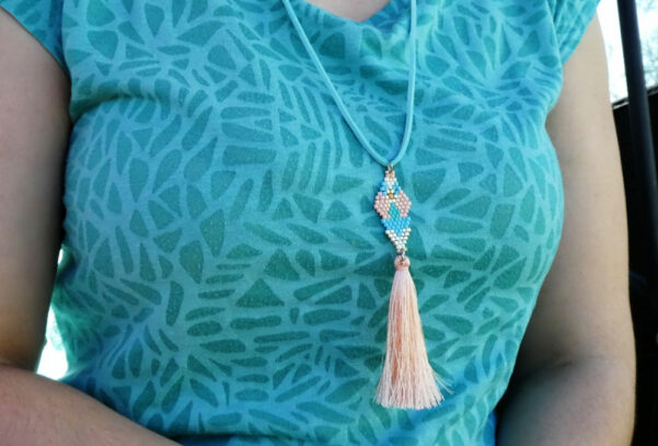 Photo porté du collier pastel tour de cou en suedine, tissage en perles miyukis terminé par un pompon couleur saumon